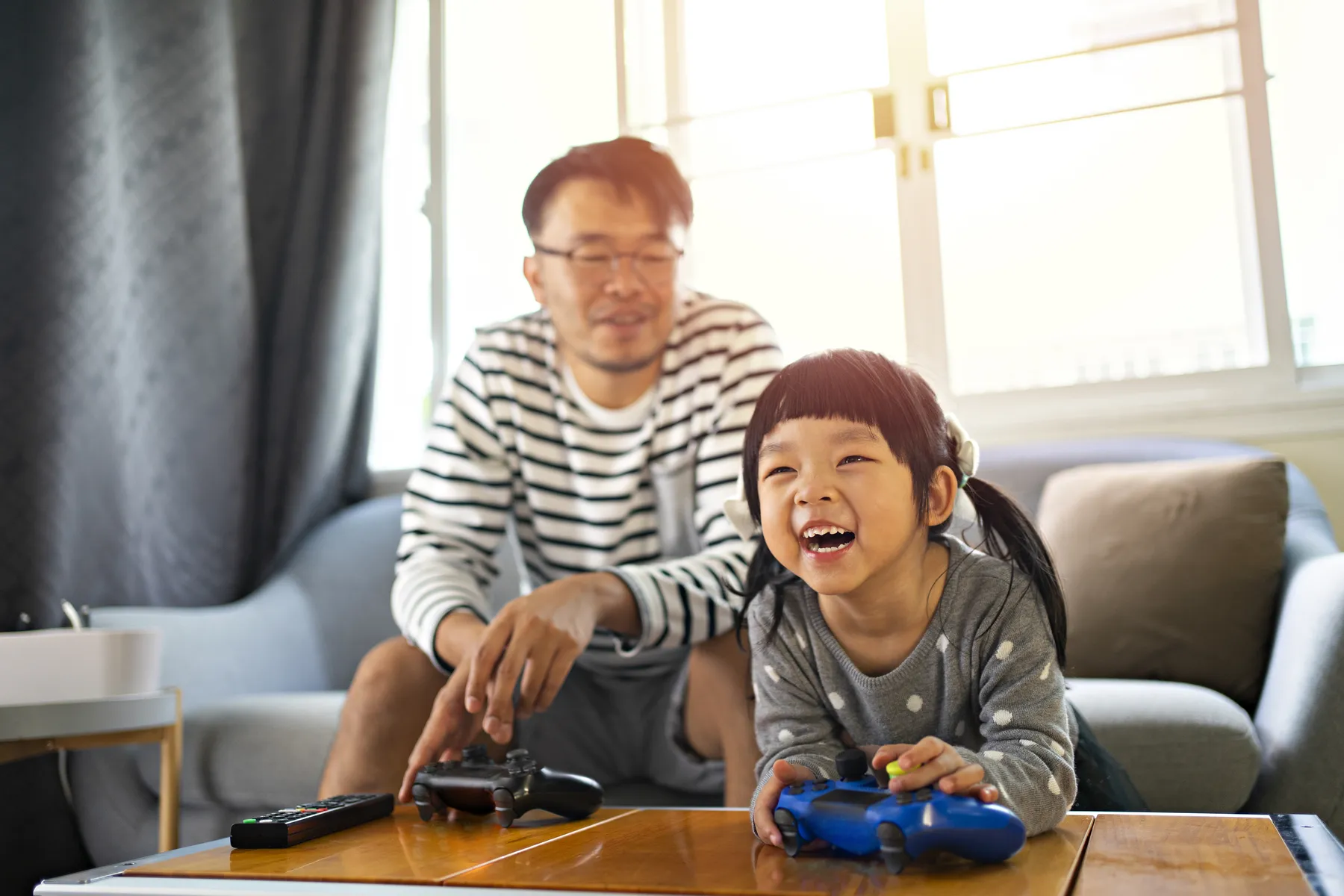Laughing young girl playing video games with her father in the living room