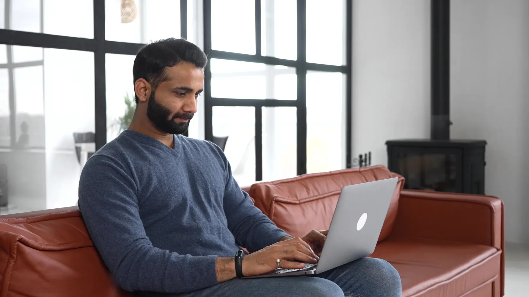 Man typing on a laptop while relaxing on a leather sofa