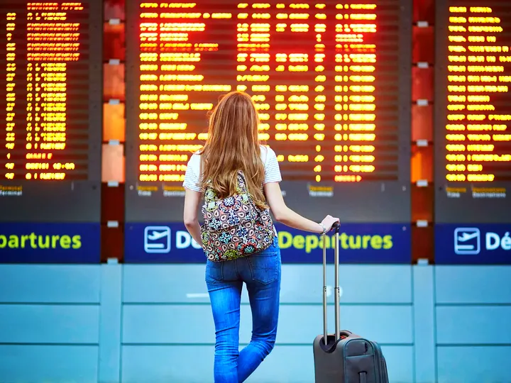 Traveller with a suitcase looking at an airport departures board