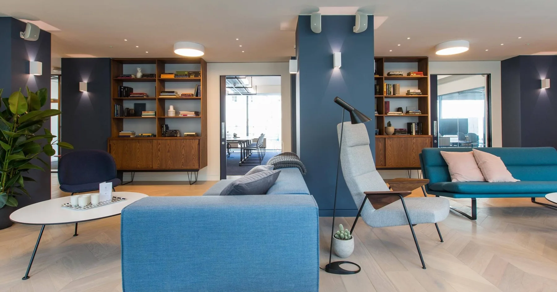 Office lounge with blue sofas, a grey armchair and wooden bookshelves