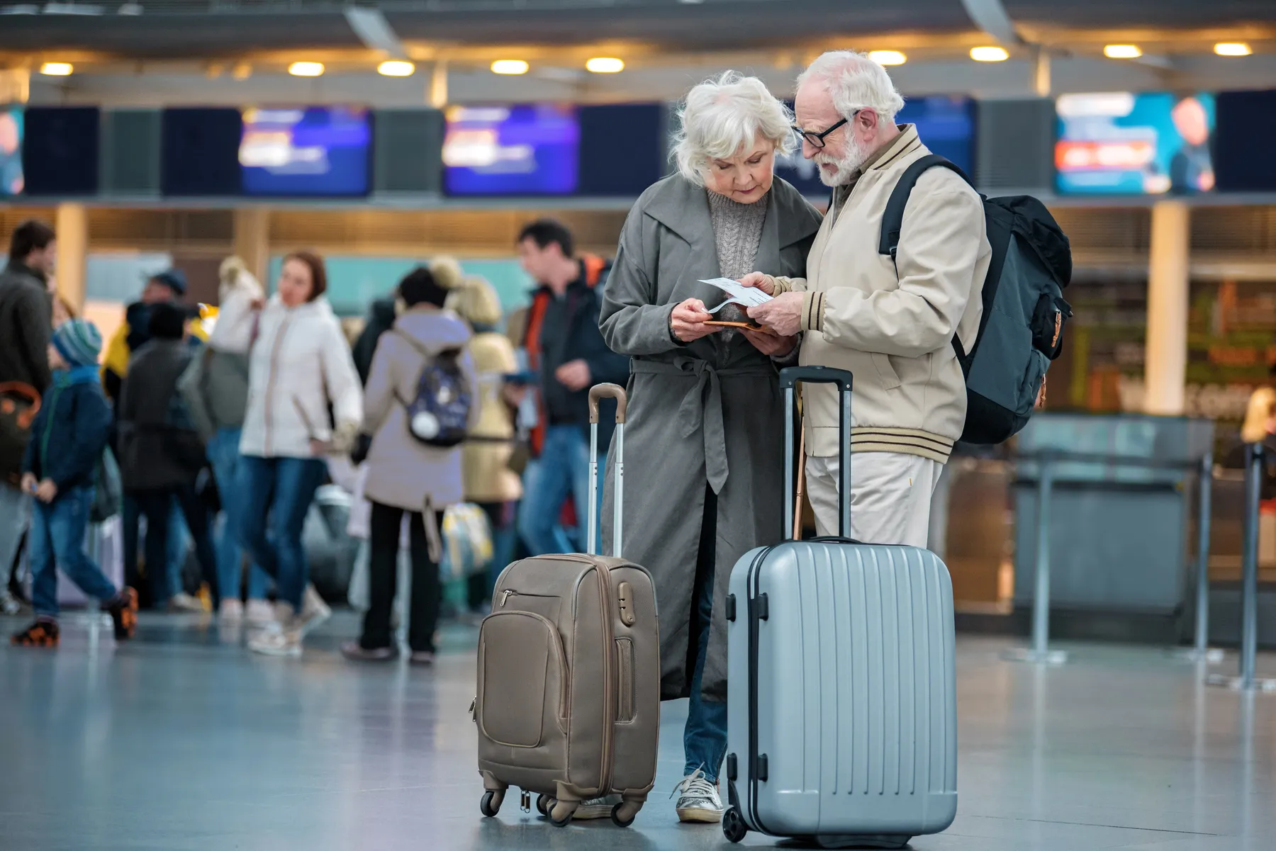 Older couple with suitcases checking travel documents in an airport terminal