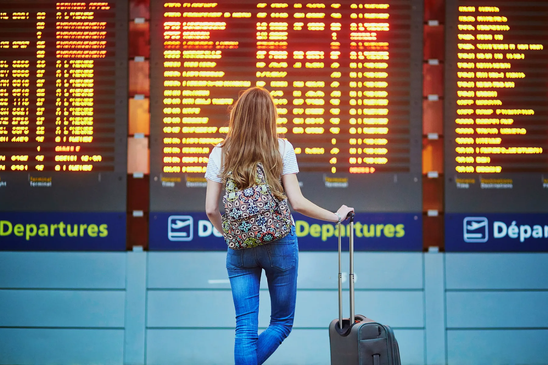 Traveller with a suitcase looking at an airport departures board