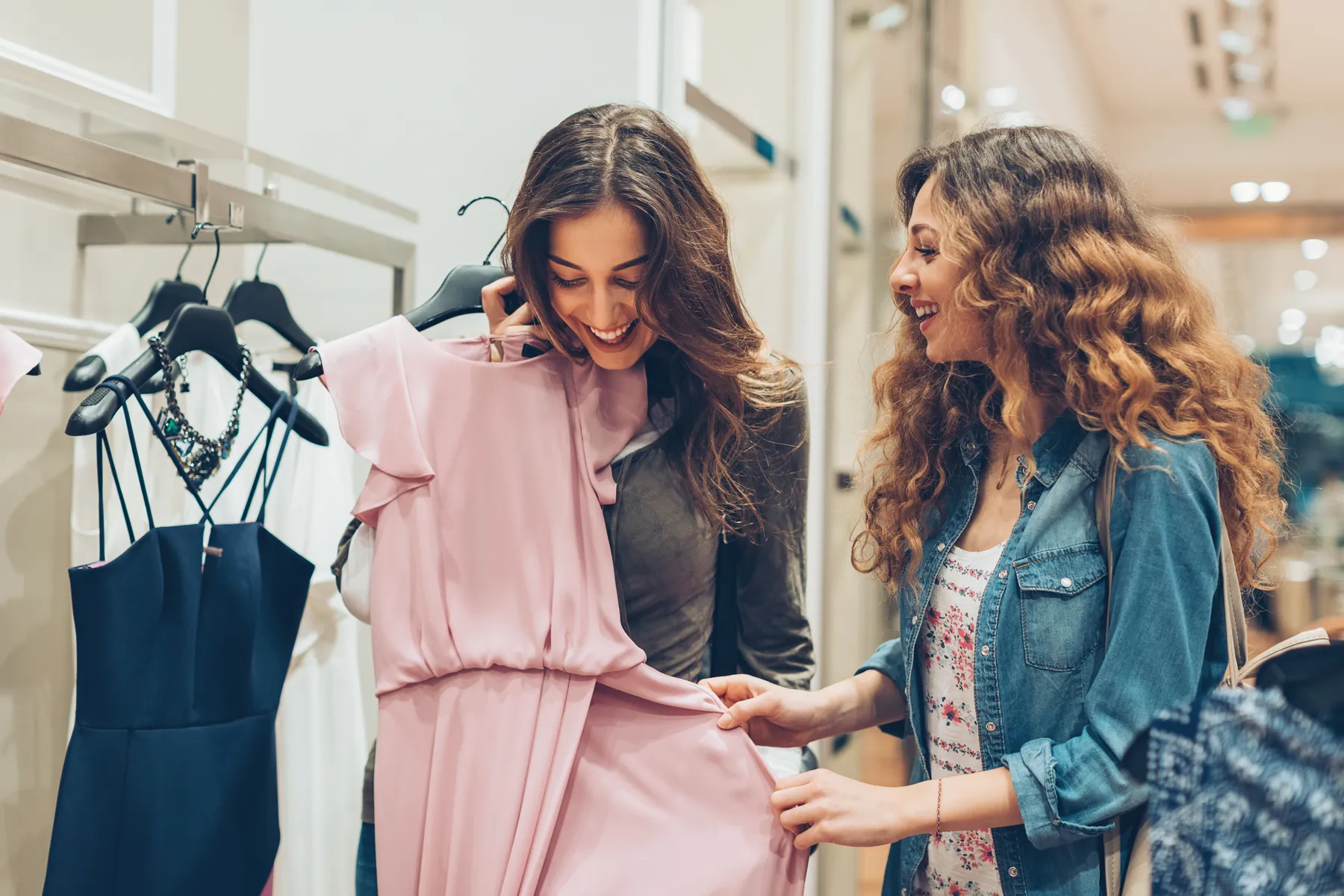 Two friends laughing while choosing a pink dress in a clothes shop