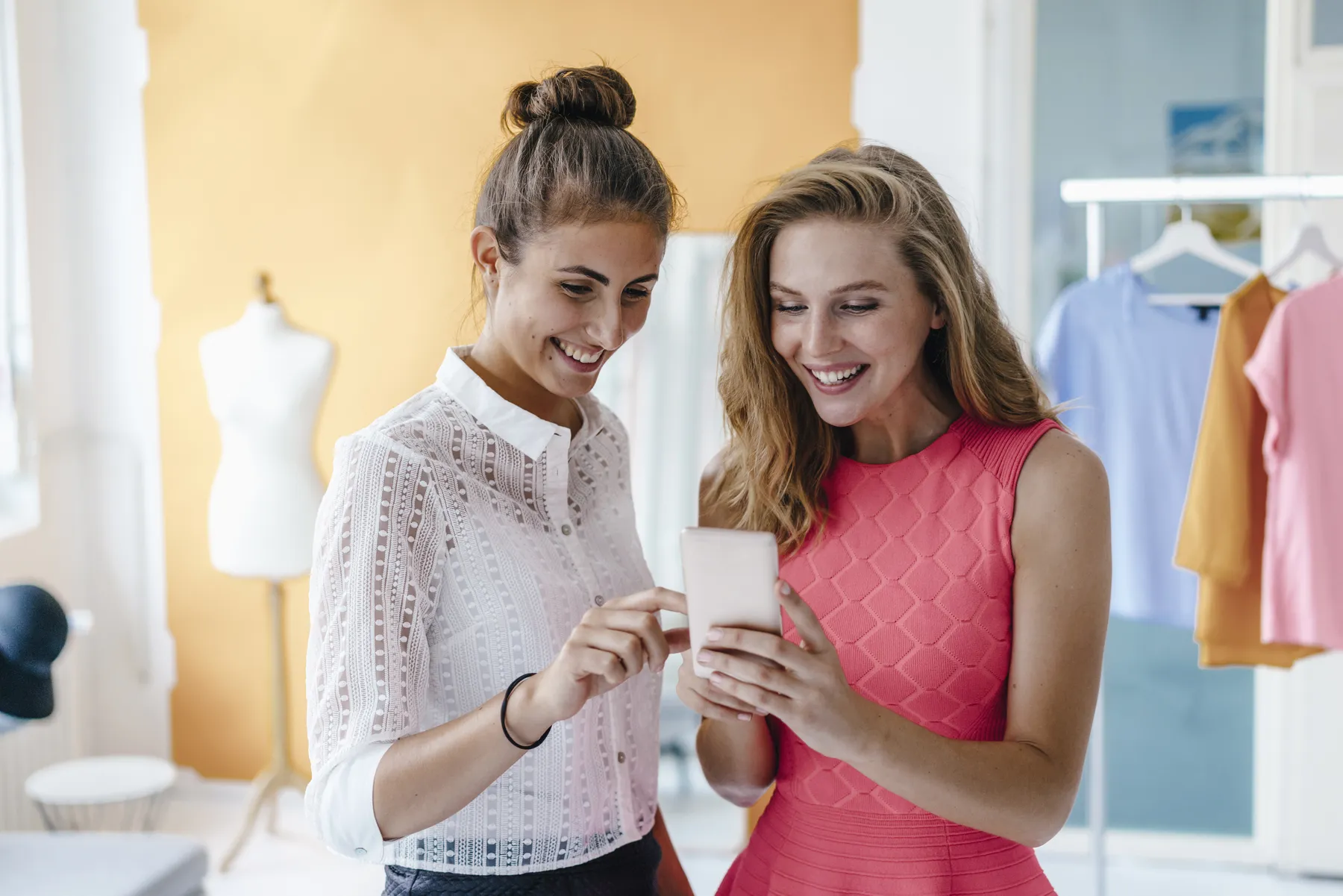 Two smiling women looking at a phone together in a fashion boutique