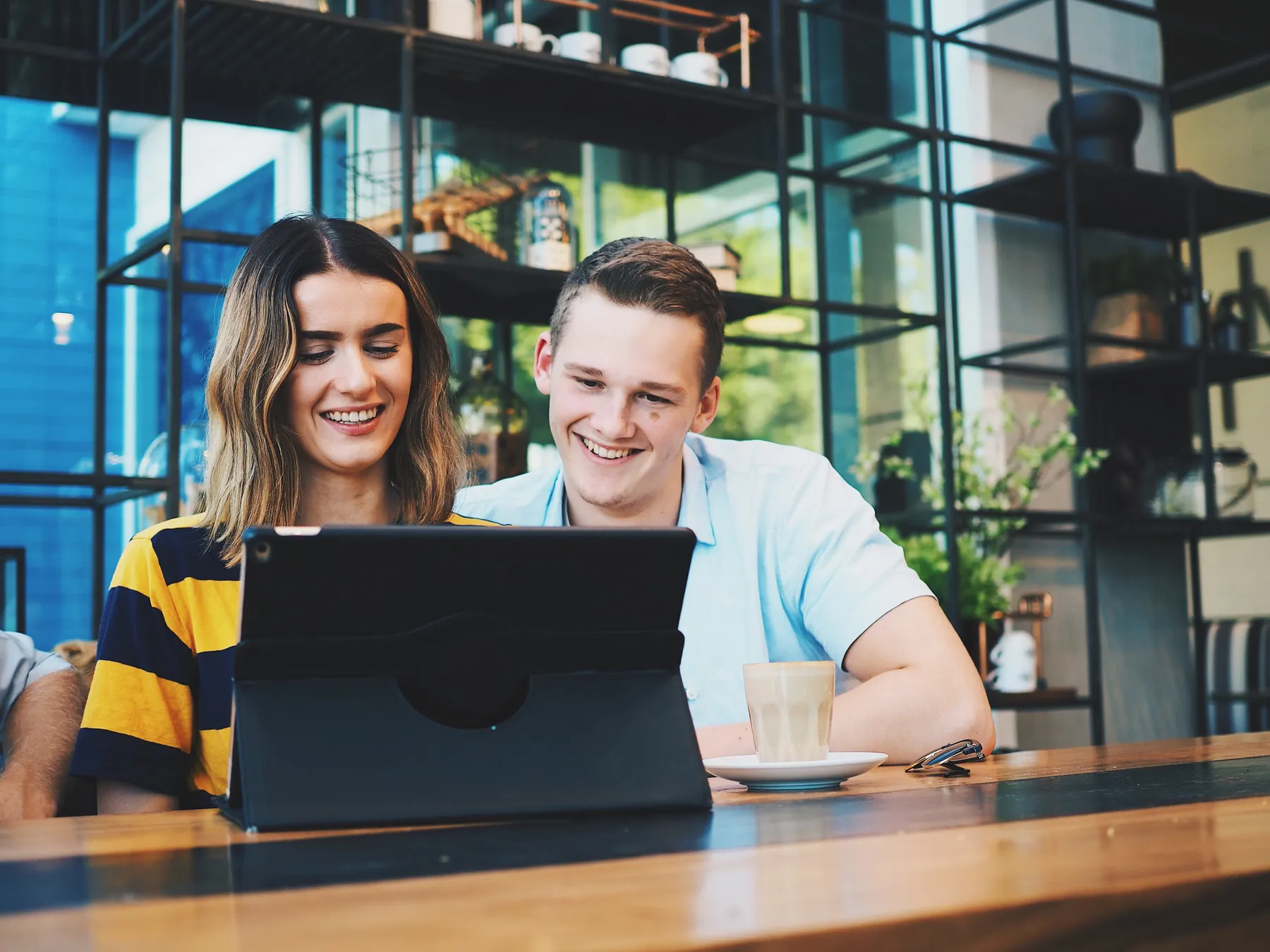 Two young people smiling at a tablet in a café