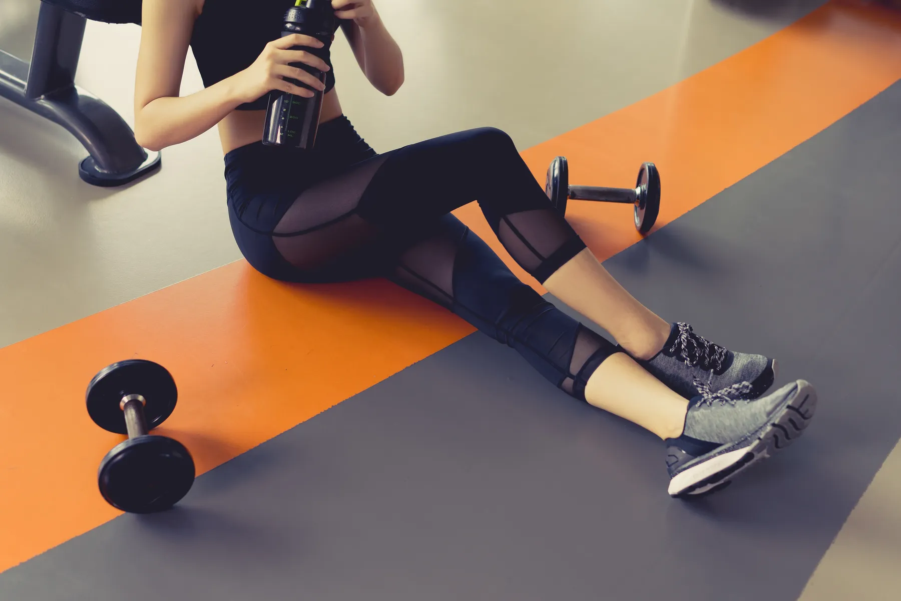 Woman resting on a gym floor with a water bottle and dumbbells